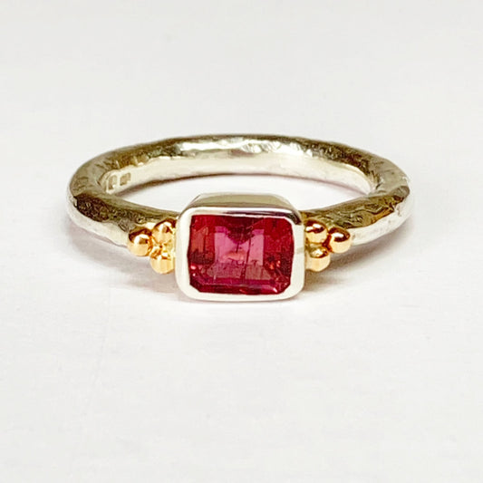 A warm rectangular pink tourmaline is the centrepiece as it sits in the polished bezel setting on a contrasting gently hammered 2.5mm silver shank with 9ct gold beading on the shoulders. Unique and handcrafted at the workbench. Amanda Cox for Heart Gallery