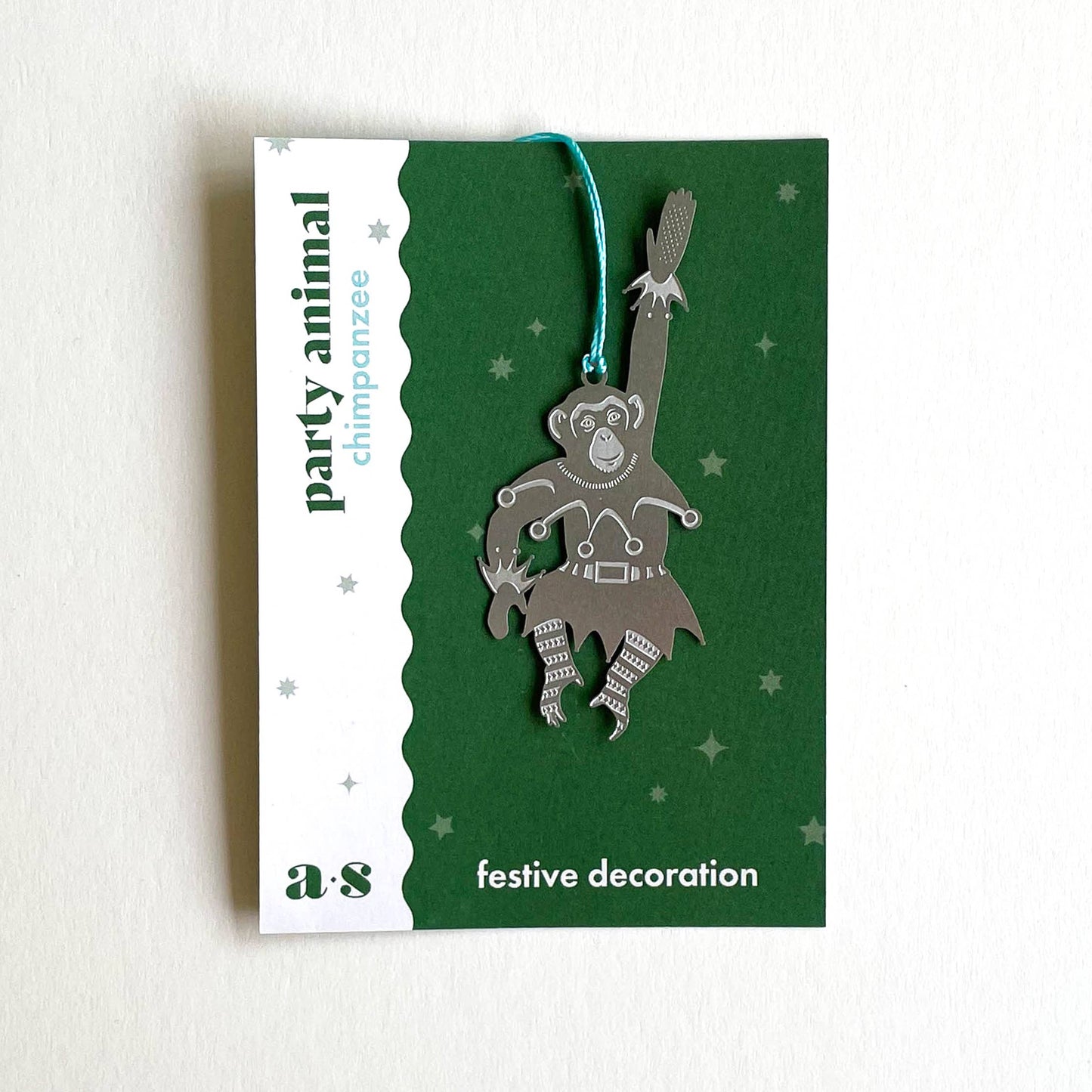 A stainless steel chimpanzee-shaped Christmas ornament hanging from a blue cord, by Another Studio for Heart Gallery