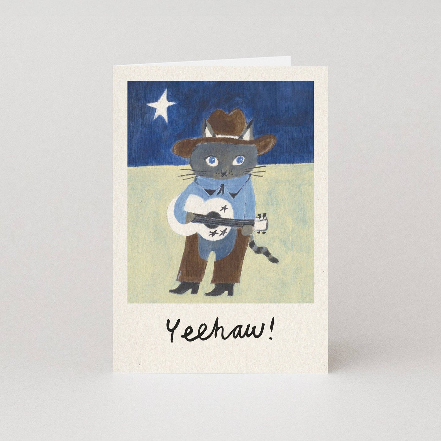Card with an illustration of a cat in cowboy attire playing a guitar under a starry sky.