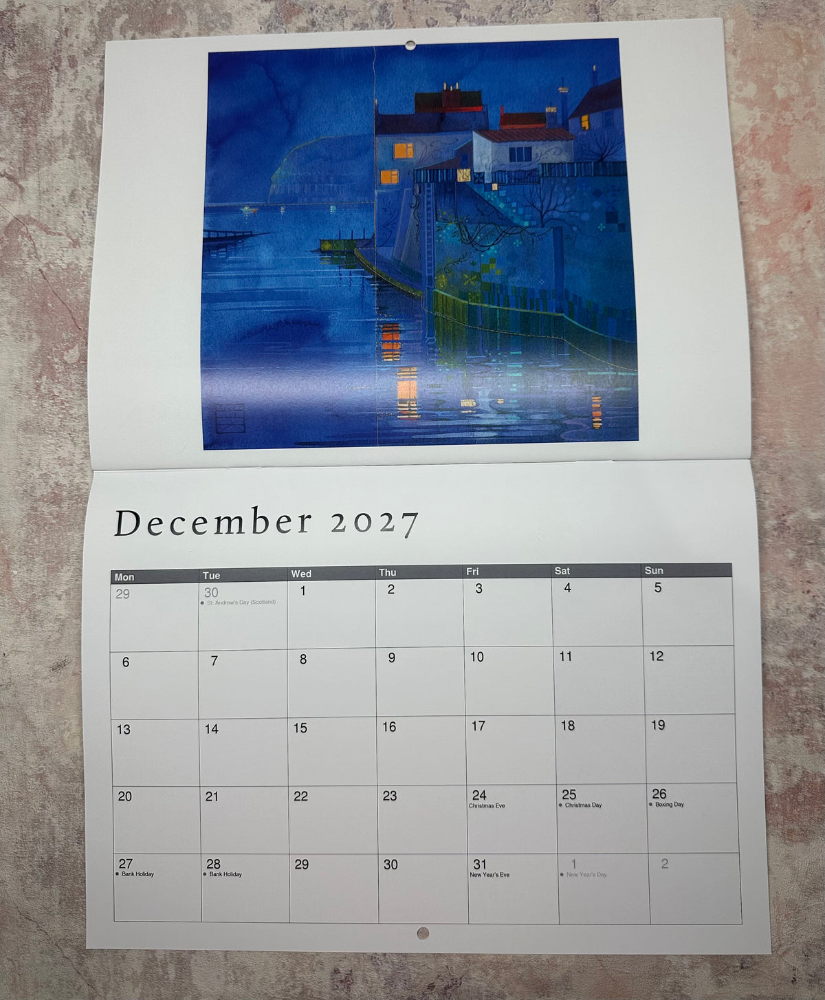 A hanging wall calendar page from Kate Lycett's 2027 calendar showing the month December 2027, with Staithes at Nightabove the calendar grid. Available from Heart Gallery Hebden Bridge