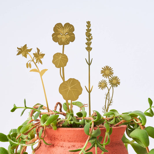 A set of brass plant decorations in the shapes of various flowers placed atop a pot with greenery.