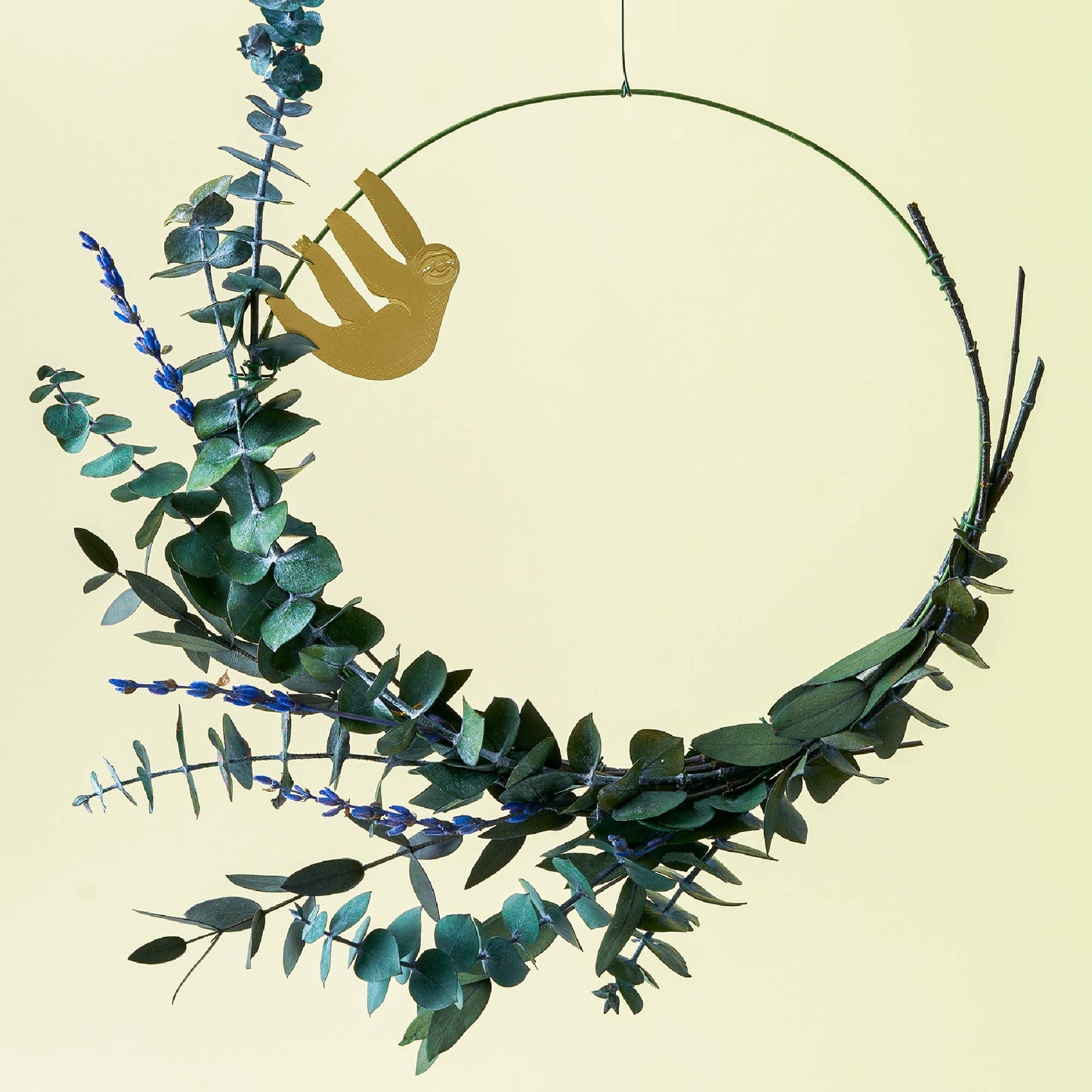 Decorative wreath with green leaves and a brass sloth figure on a beige background