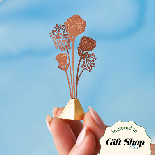 A hand holding a small decorative bouquet with copper flowers on a blue background, with a 'featured in Gift Shop' label at the bottom.