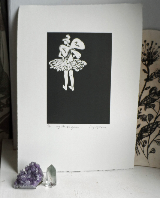 A signed and titled original linocut print by Polly Marix-Evans, depicting a fairy, mounted on white paper. The artwork is displayed with a crystal and a floral patterned object in the background.