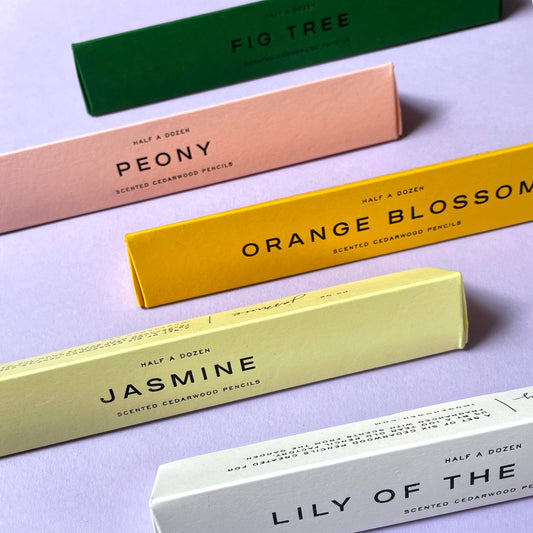 Colorful boxes of scented cedarwood pencils on a light purple background by Imogen Owen