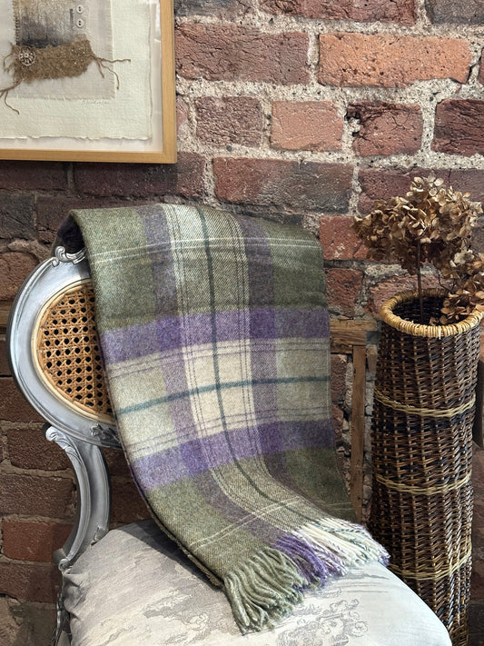 Plaid blanket draped over a chair against a brick wall with a wicker basket. Bronte Moon Skye throw for Heart Gallery