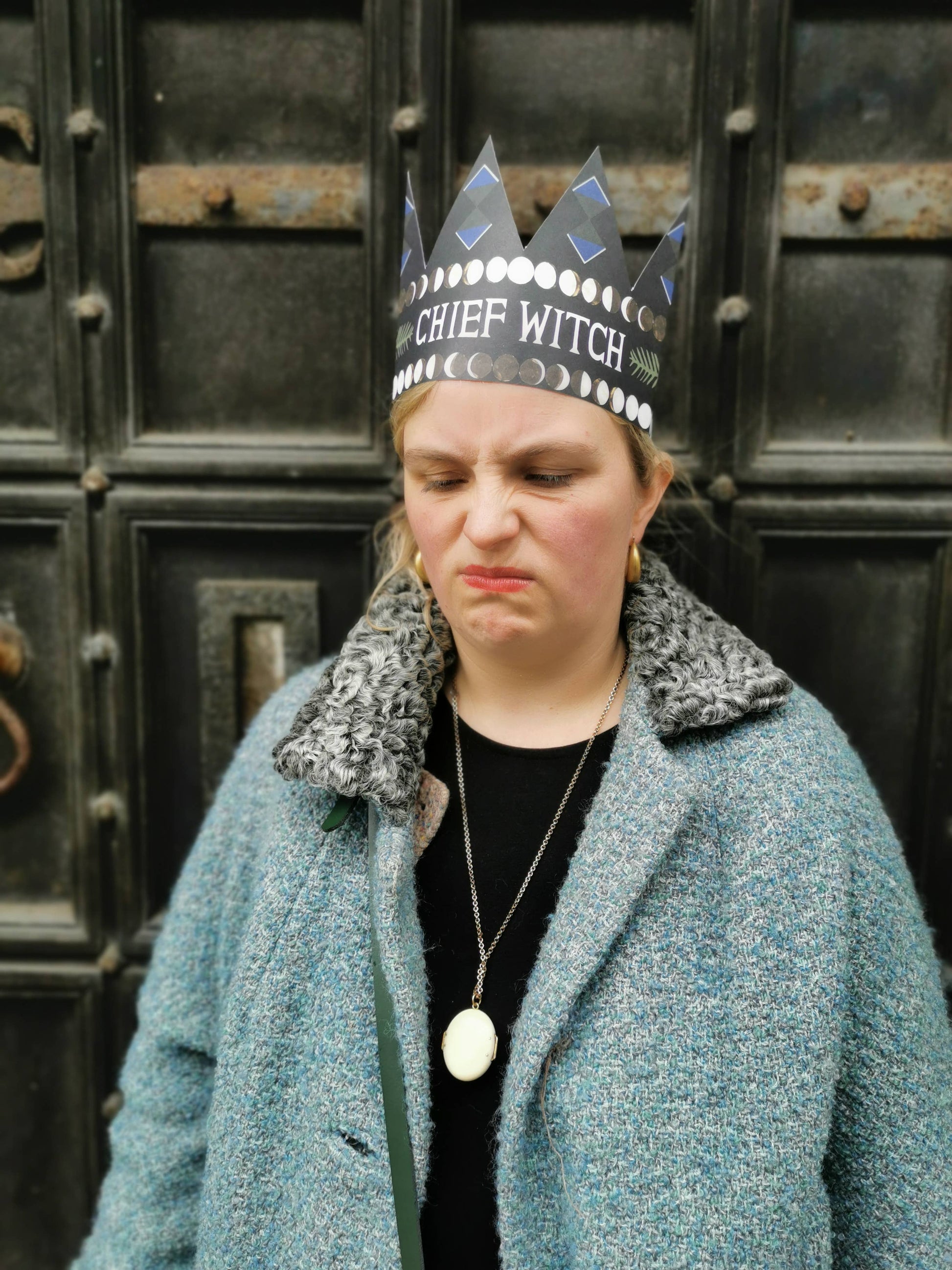 Person wearing a crown labeled 'Chief Witch' in front of a dark, textured wall.