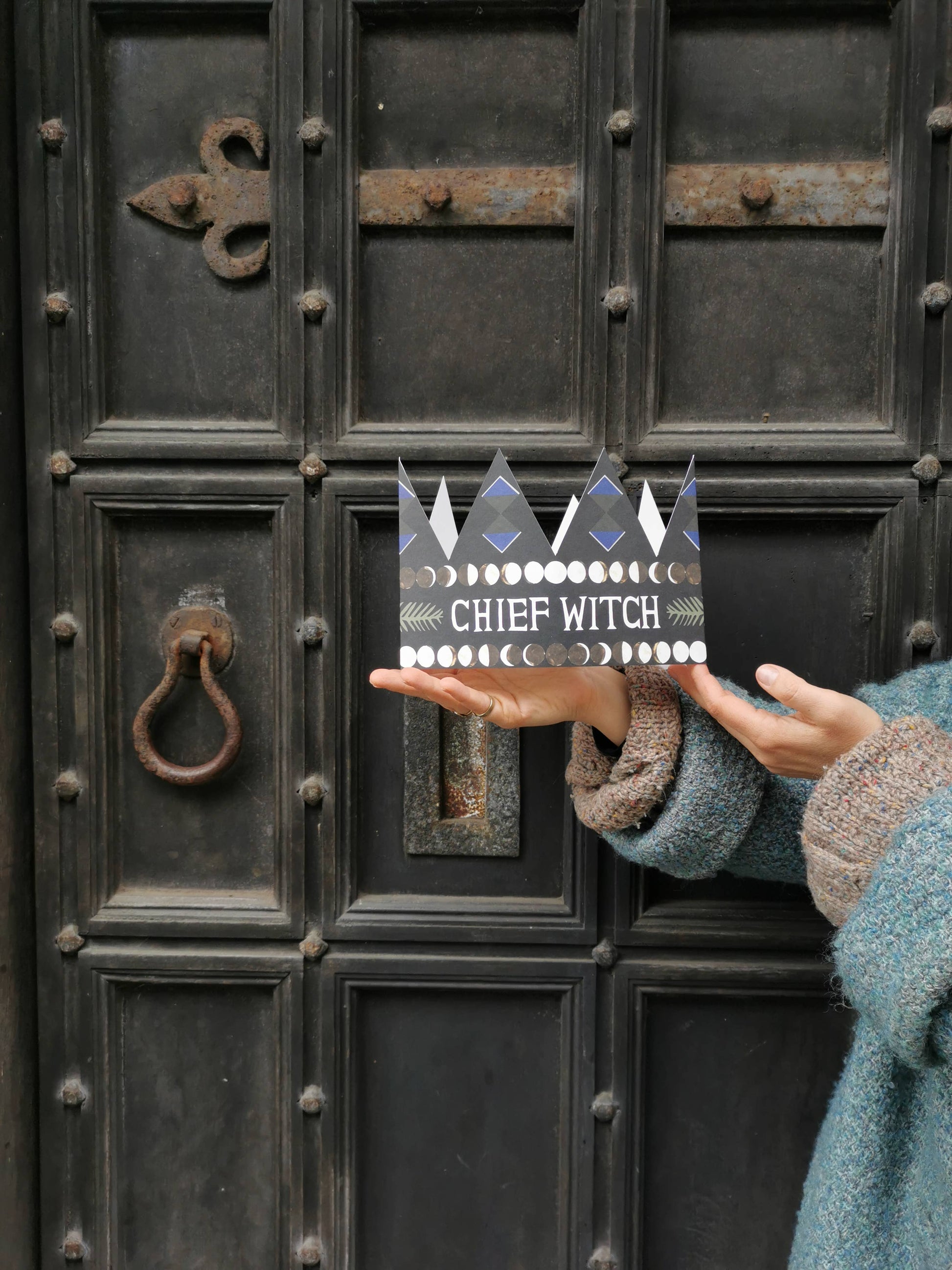 Person holding a card with 'Chief Witch' text in front of an old door