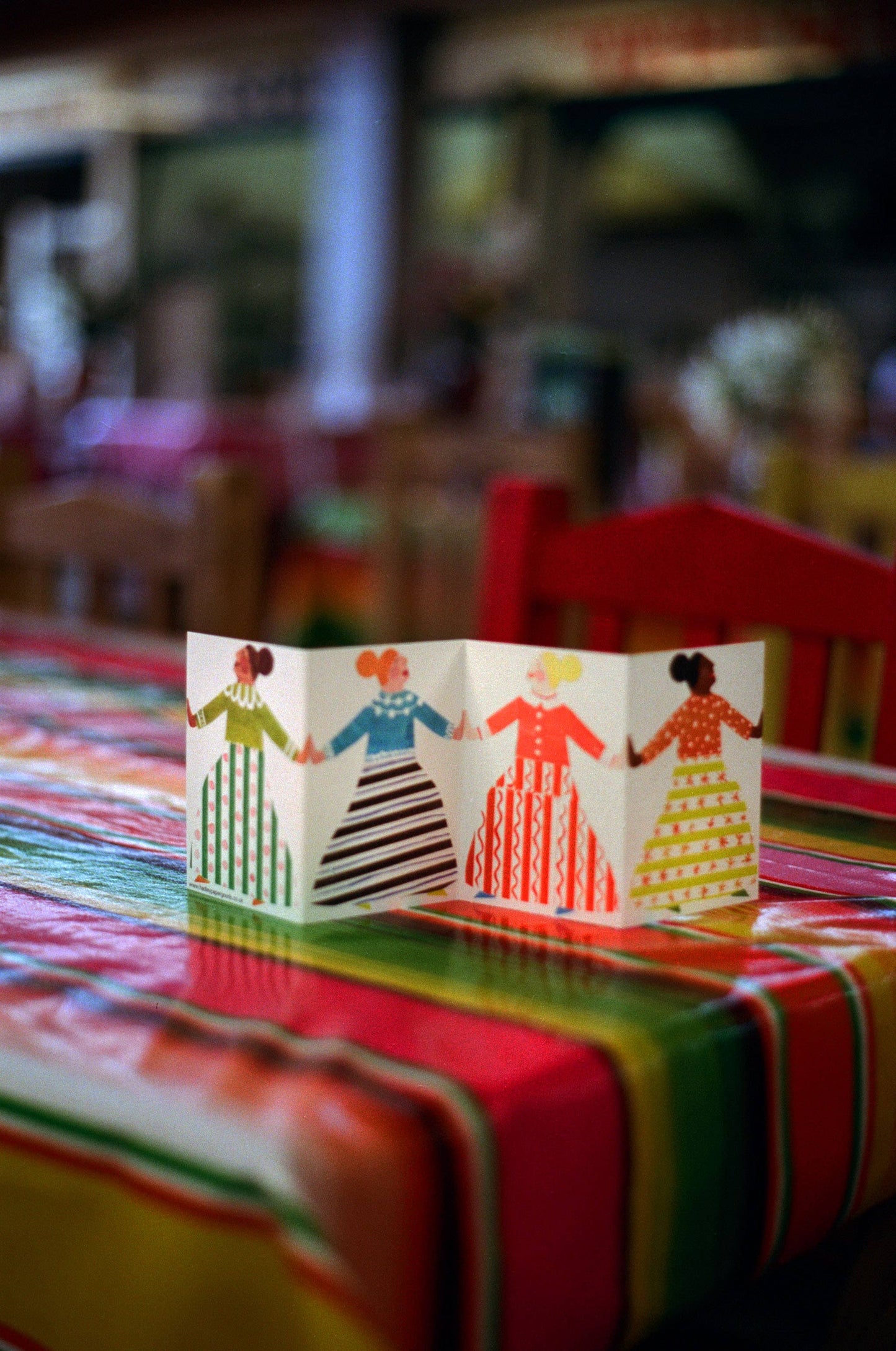Colorful paper cutout of four people on a table with a blurred restaurant background
