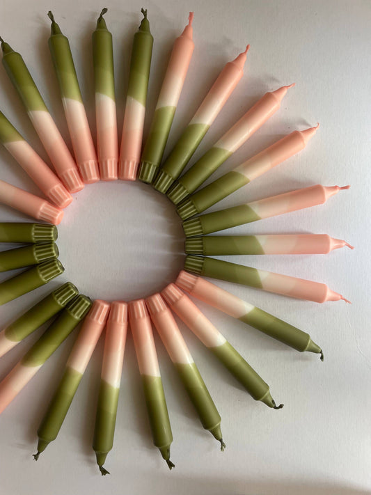A set of blush pink and olive green dip dyed dinner candles arranged in a circle on a white surface.