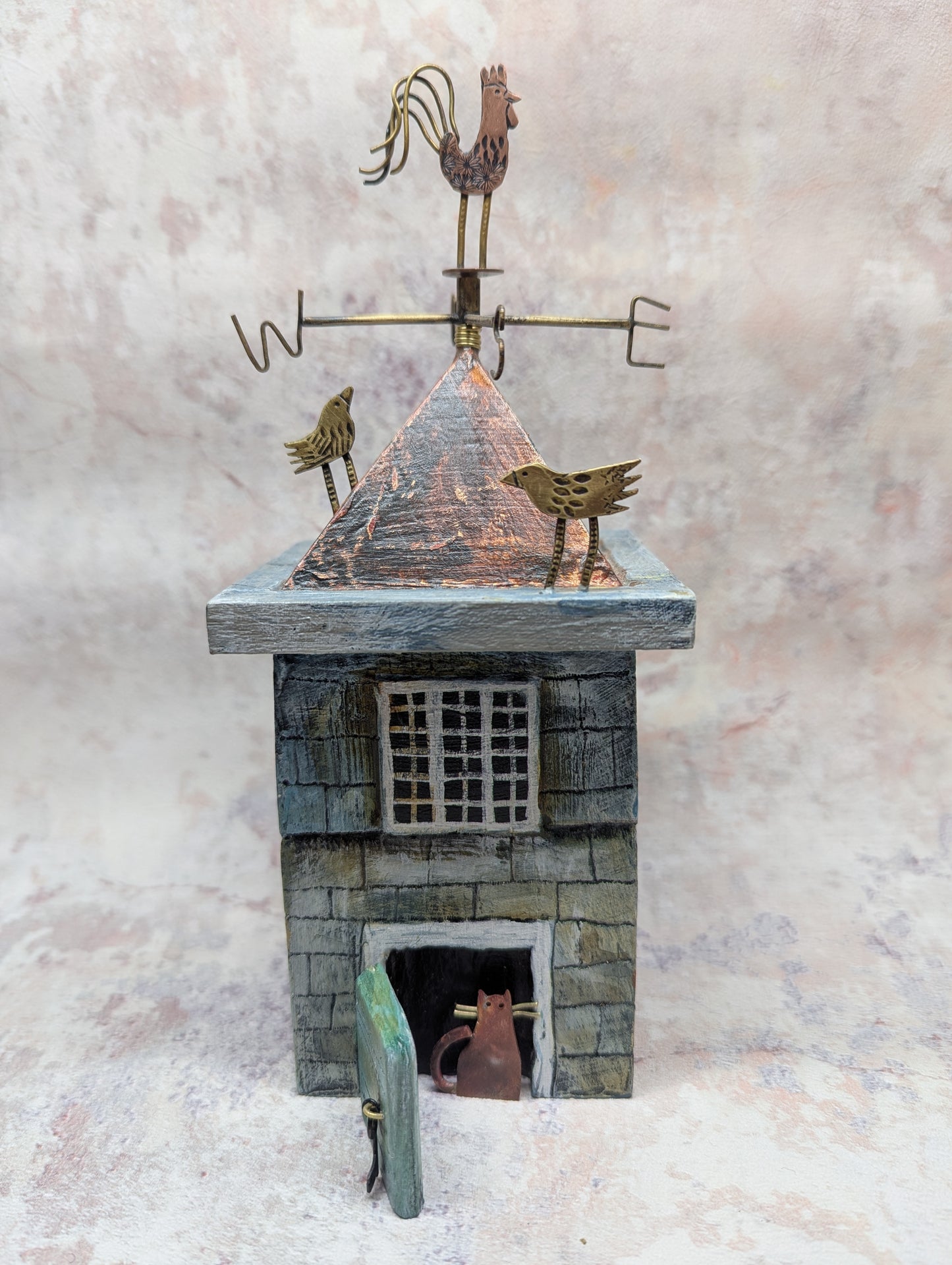 Small building with a weathervane and a cat inside on a textured gray background