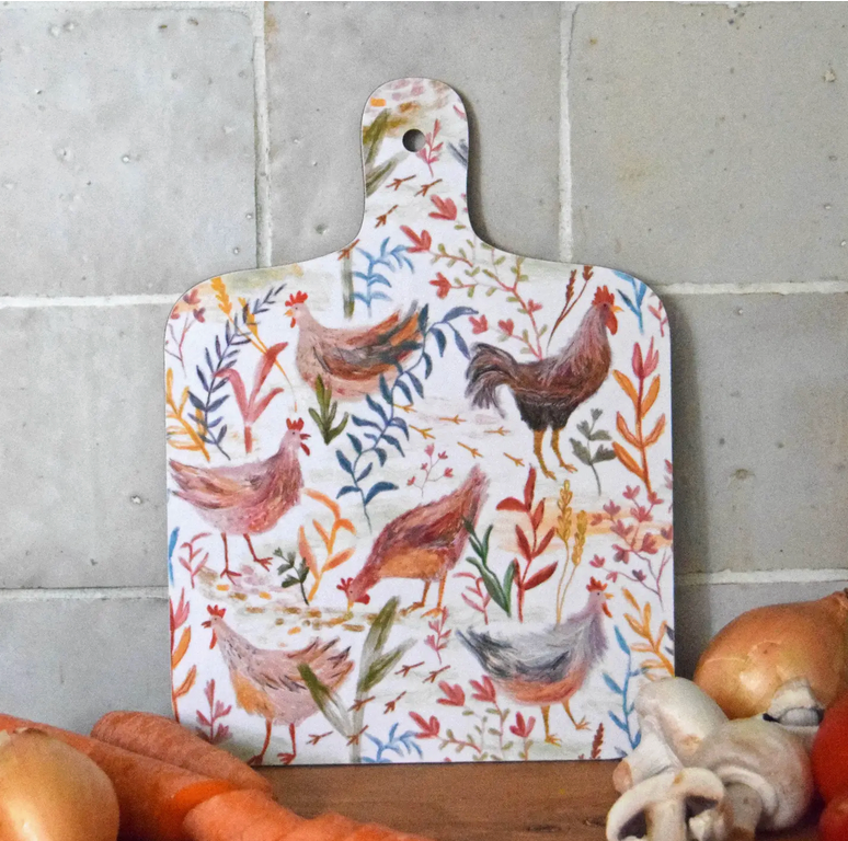 A decorative mini chopping board with a colorful chicken pattern on a white background, displayed on a wooden surface with vegetables around it.