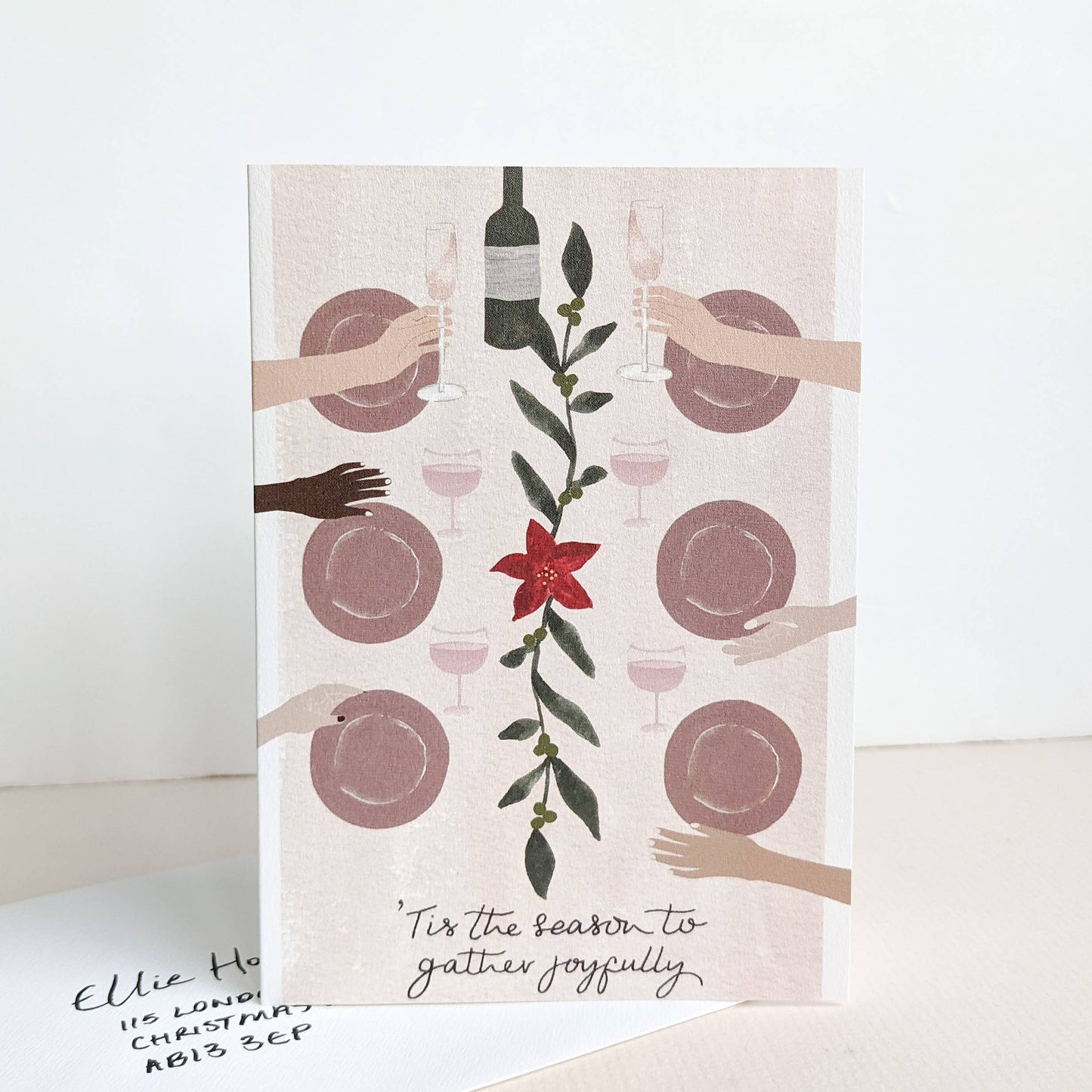 christmas card holding plates, a bottle, and glasses, and a red flower design.