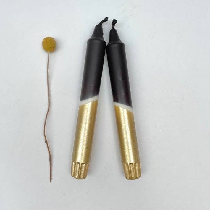 Black and gold hand dip dyed candles by The Singing Rabbit displayed next to a dried flower by The Singing Rabbit