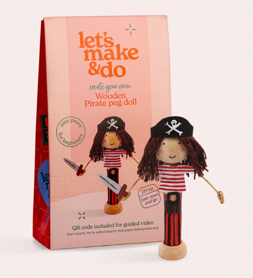 A wooden pirate peg doll stands in front of its pink packaging box. The box reads 'let's make & do' and 'create your own Wooden Pirate peg doll.