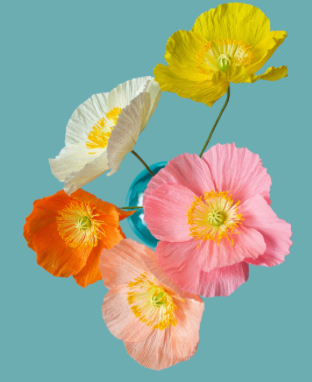 Five paper poppy flowers in yellow, pink, peach, orange, and white, arranged in a small blue vase against a solid teal background.