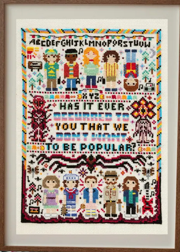 Cross-stitched sampler with characters and text, framed in a wooden border.