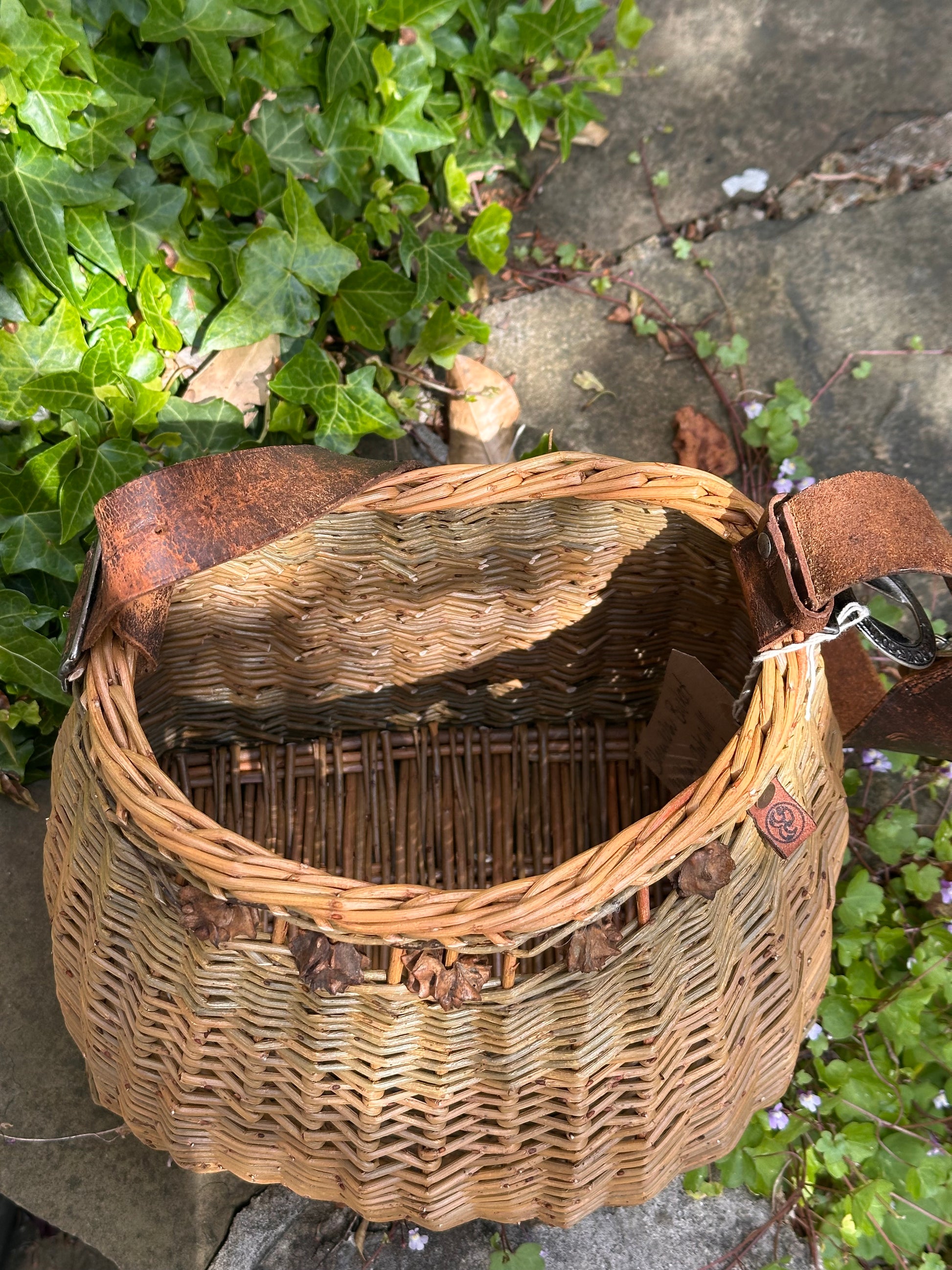 Willow basket with a leather scout belt on a stone surface with greenery in the background