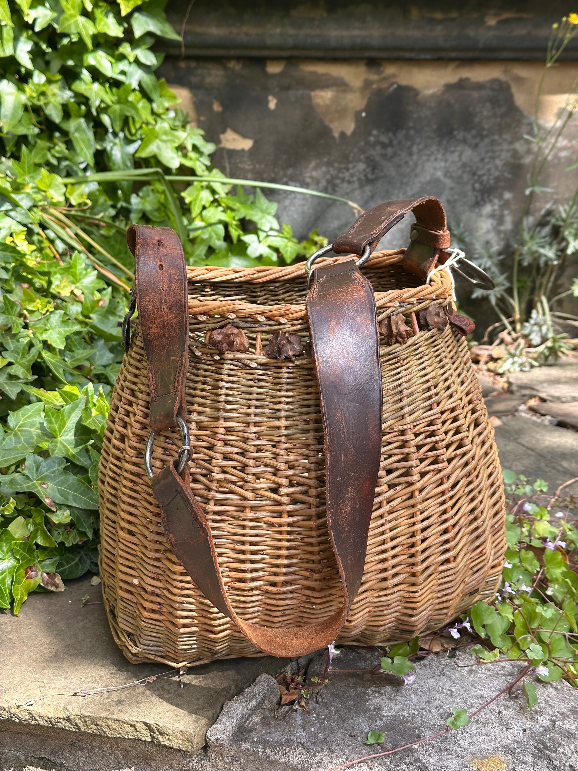 Willow basket with leather straps on a stone surface with greenery in the background