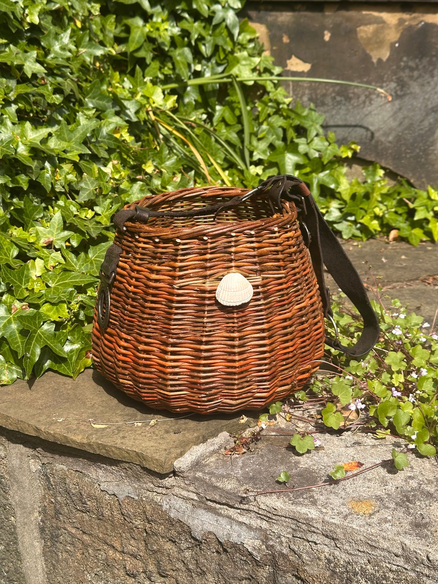 Willow  basket with a strap on a stone ledge with greenery in the background
