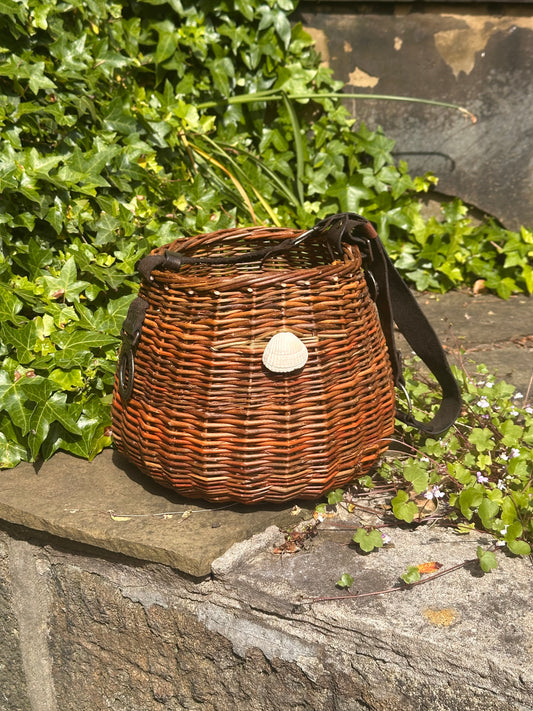 Willow  basket with a strap on a stone ledge with greenery in the background