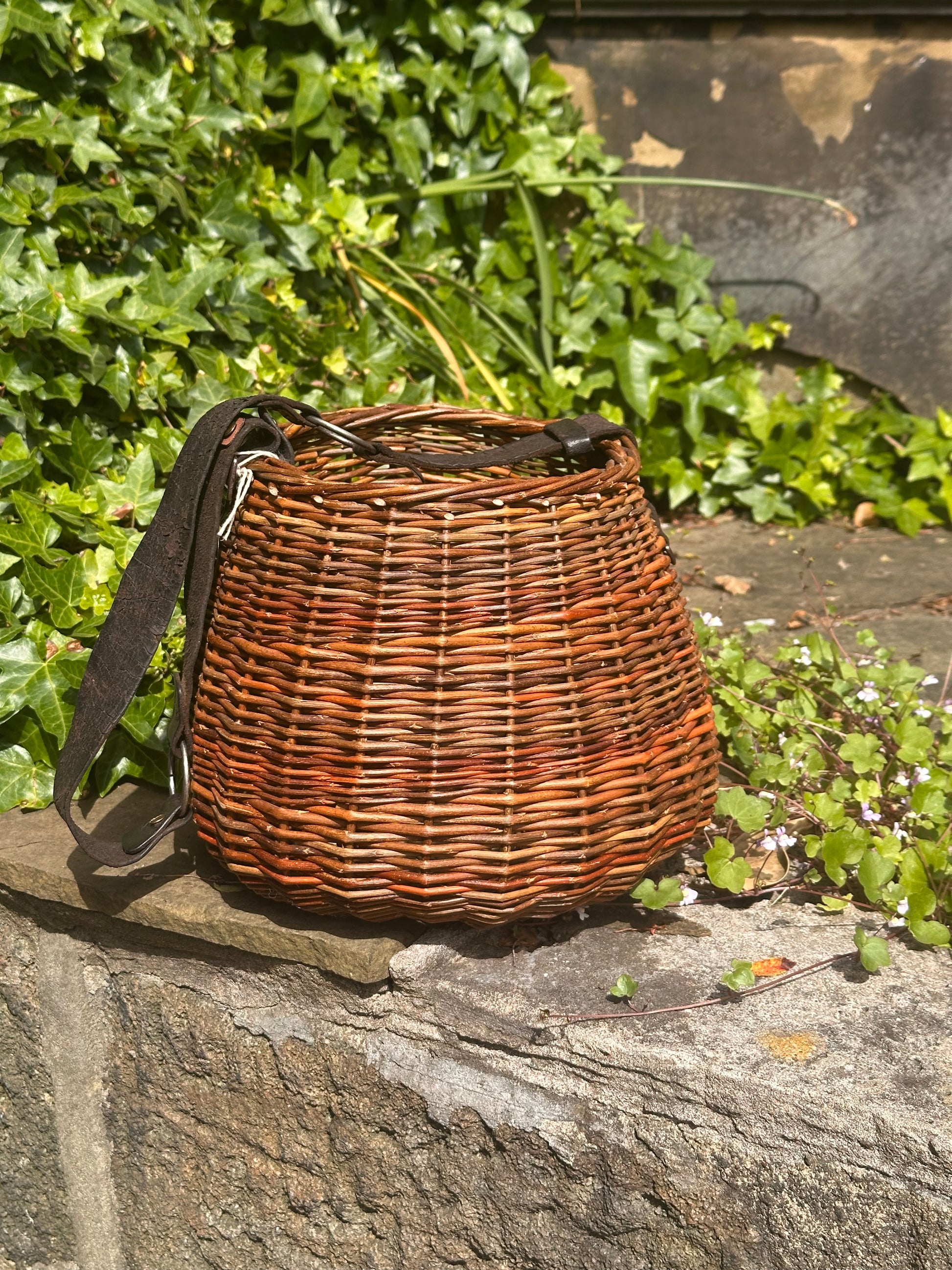 Willow basket with a strap on a stone surface with greenery in the background