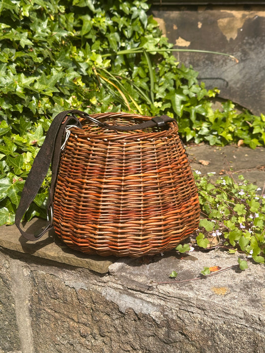 Willow basket with a strap on a stone surface with greenery in the background