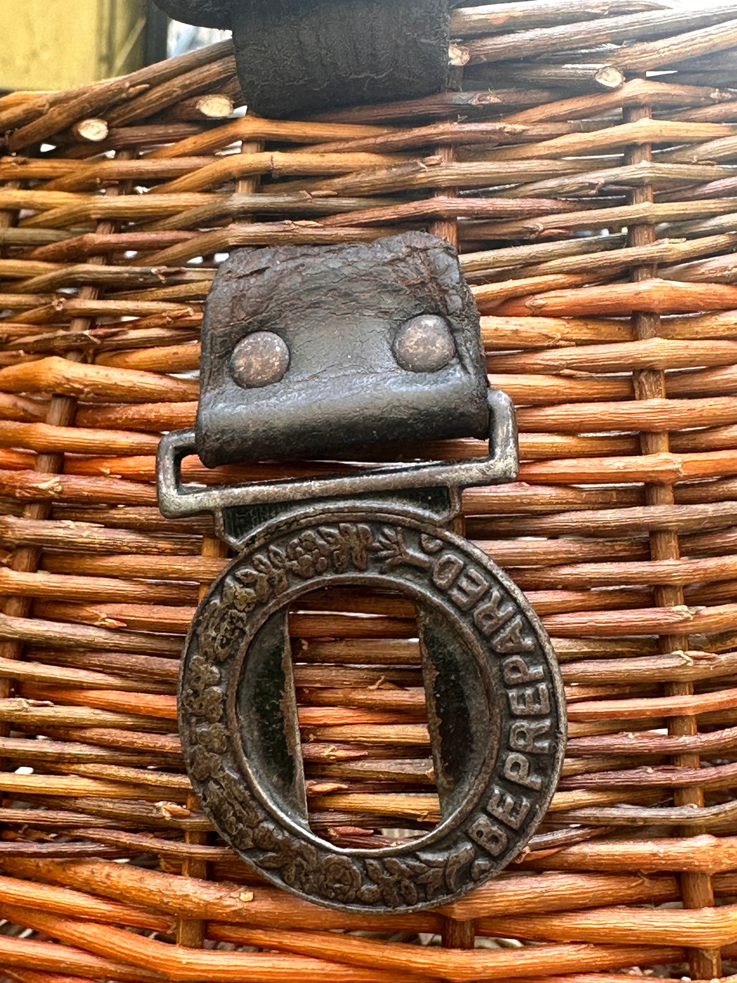 Close-up of a willow basket with a metal buckle and 'Be Prepared' engraving.