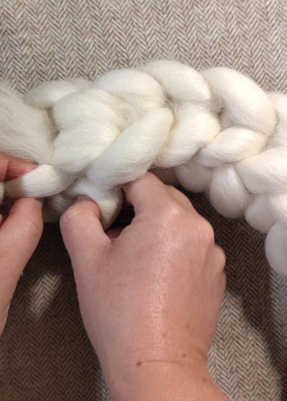A close-up of a Sophie's hands holding and stretching a thick, fluffy white braid of wool to make a festive wreath at Heart Gallery Hebden Bridge