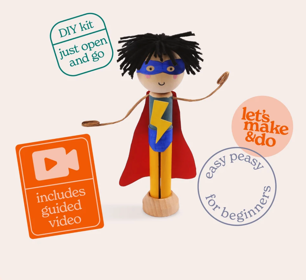 DIY wooden superhero toy set featuring a wooden figure with black yarn hair, a red cape, blue mask, and yellow lightning-bolt chest emblem, shown on a light beige background with promotional badges.