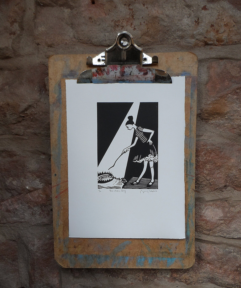 Original Linocut artwork mounted on a clipboard, depicting a black and white illustration of a person with a bun on their head, against a textured wall background.