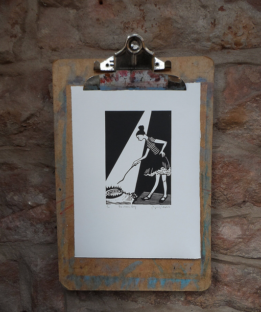 Original Linocut artwork mounted on a clipboard, depicting a black and white illustration of a person with a bun on their head, against a textured wall background.