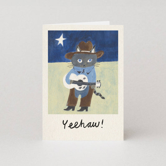 Card with an illustration of a cat in cowboy attire playing a guitar under a starry sky.