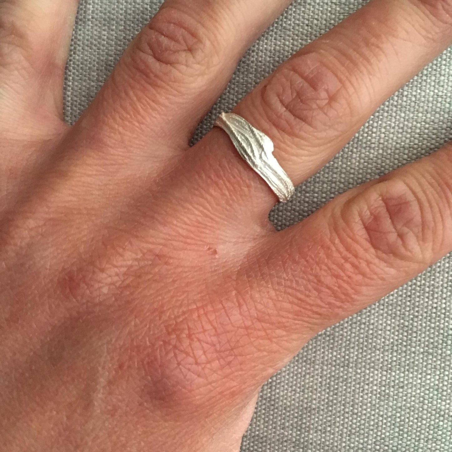 Hand wearing a silver ring on a textured gray background